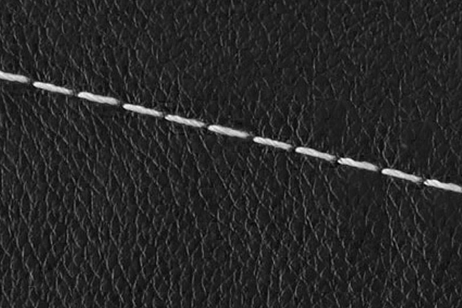 Close-up of black textured leather with a single line of white Thick Contrast Stitching running diagonally across the surface.