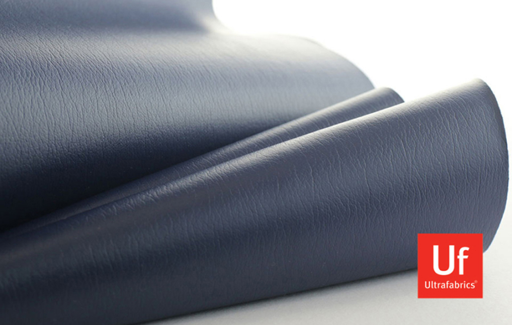 Close-up of folded navy blue leatherette with a fine, natural grain and smooth surface, creating soft curves and shadows that highlight the material’s texture. A small red square logo reading “Uf Ultrafabrics” appears in the bottom-right corner, indicating the brand.