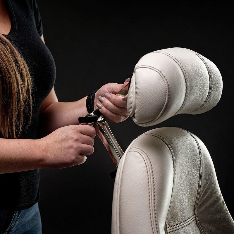 A person adjusting a light-coloured leather car seat headrest using both hands.