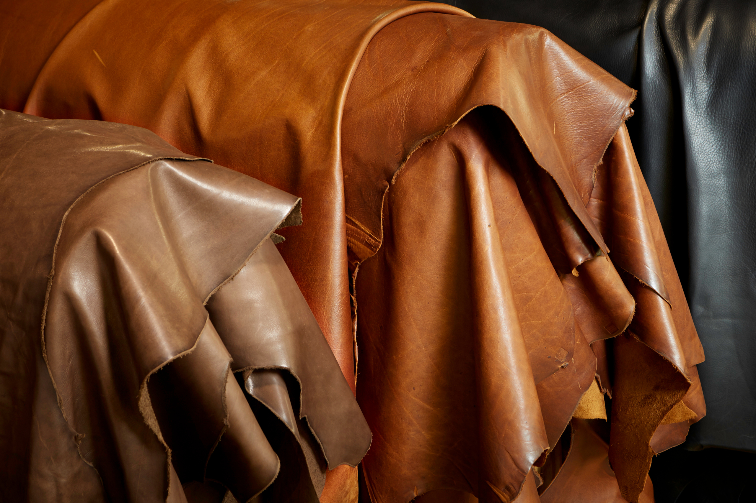 Stacks of brown and black leather hides draped over racks in a workshop.