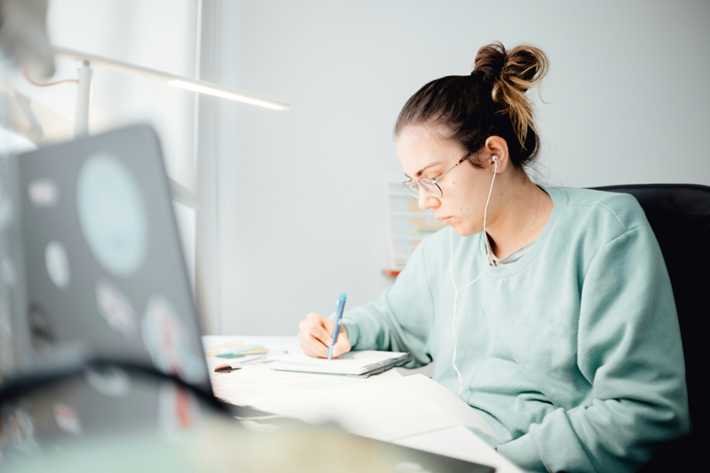 Woman sitting at a desk writing on a note pad and looking at a computer