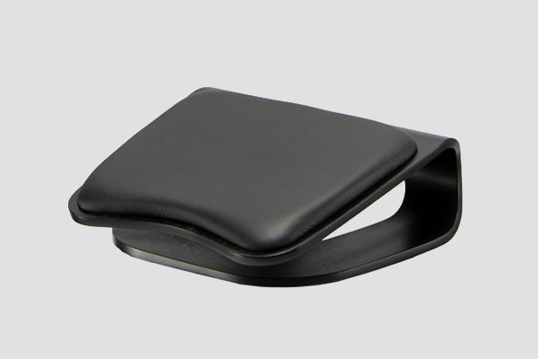 Black ergonomic footrest with curved cushioned top and arched base design shown on grey background.