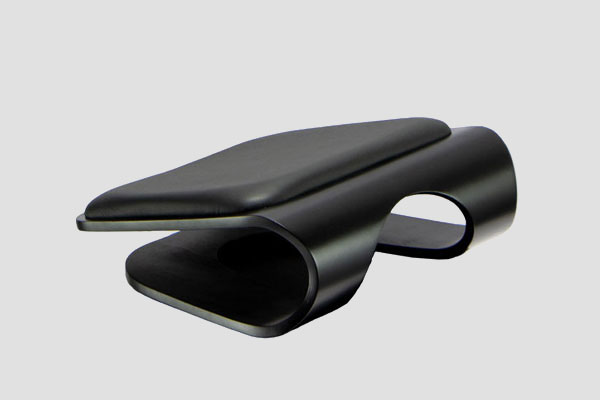 Black ergonomic footrest with curved cushioned top and arched base design shown on grey background.