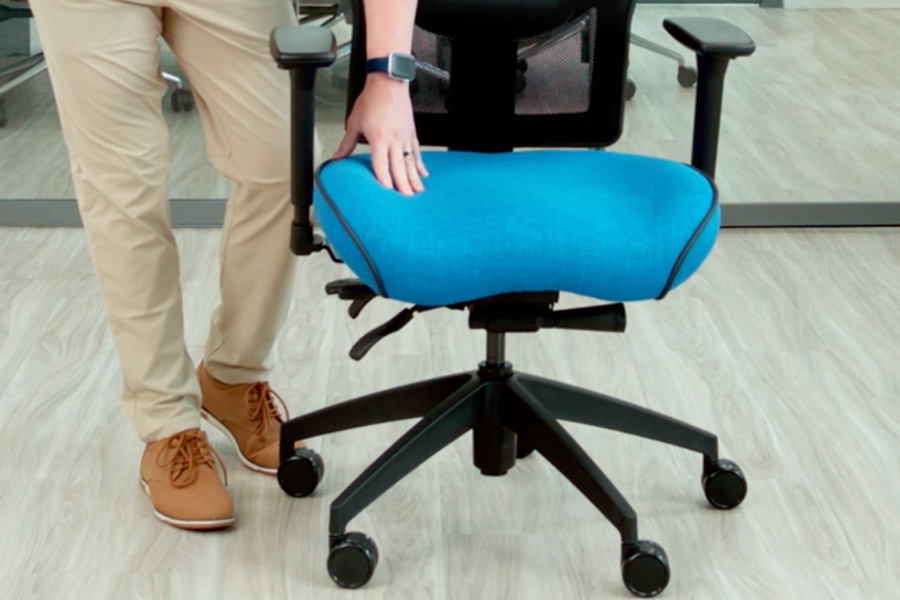 Person adjusting a blue ergonomic office chair with a mesh back and wheeled base on a light wood floor.