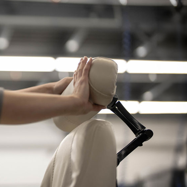 Close-up of a beige ergonomic office chair headrest with a person's hand demonstrating the adjustable headrest feature. The black adjustment lever is visible on the side, showing how users can customize neck and head support for personalized comfort and proper cervical alignment.